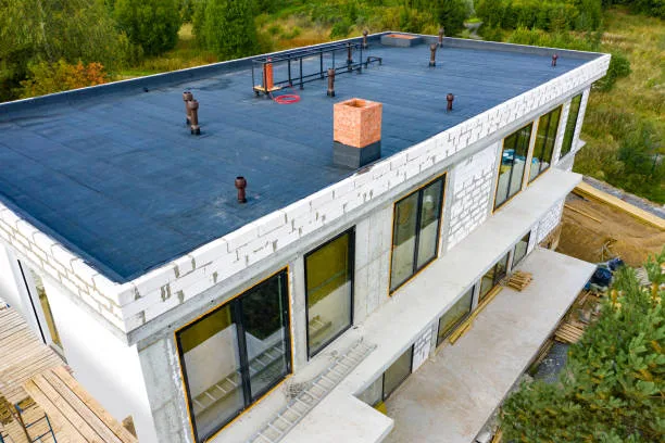 Dark low-slope roof on a small building with several roof penetrations