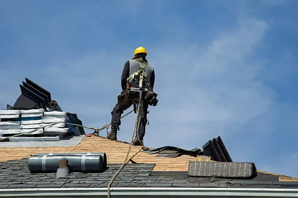 Roofer standing on a sloped roof beside roofing materials
