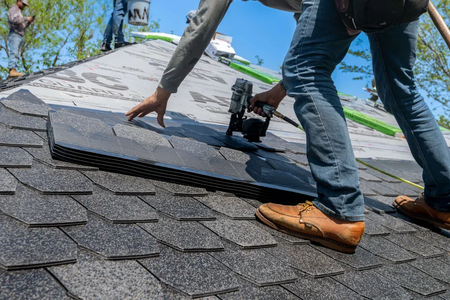 Installer fastening asphalt shingles on a sloped roof