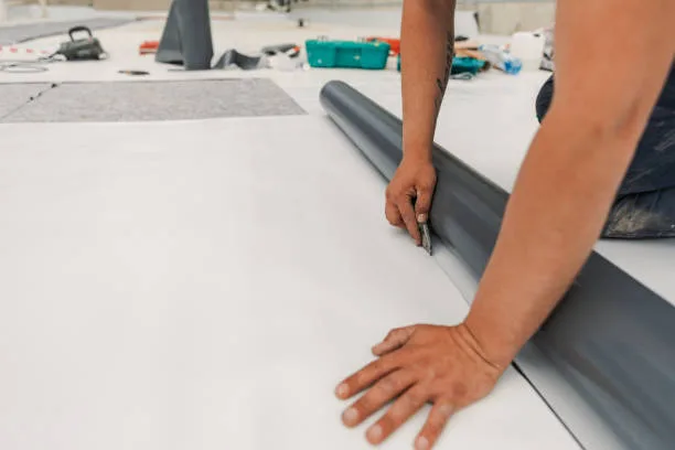 Worker cutting a white single-ply roof membrane